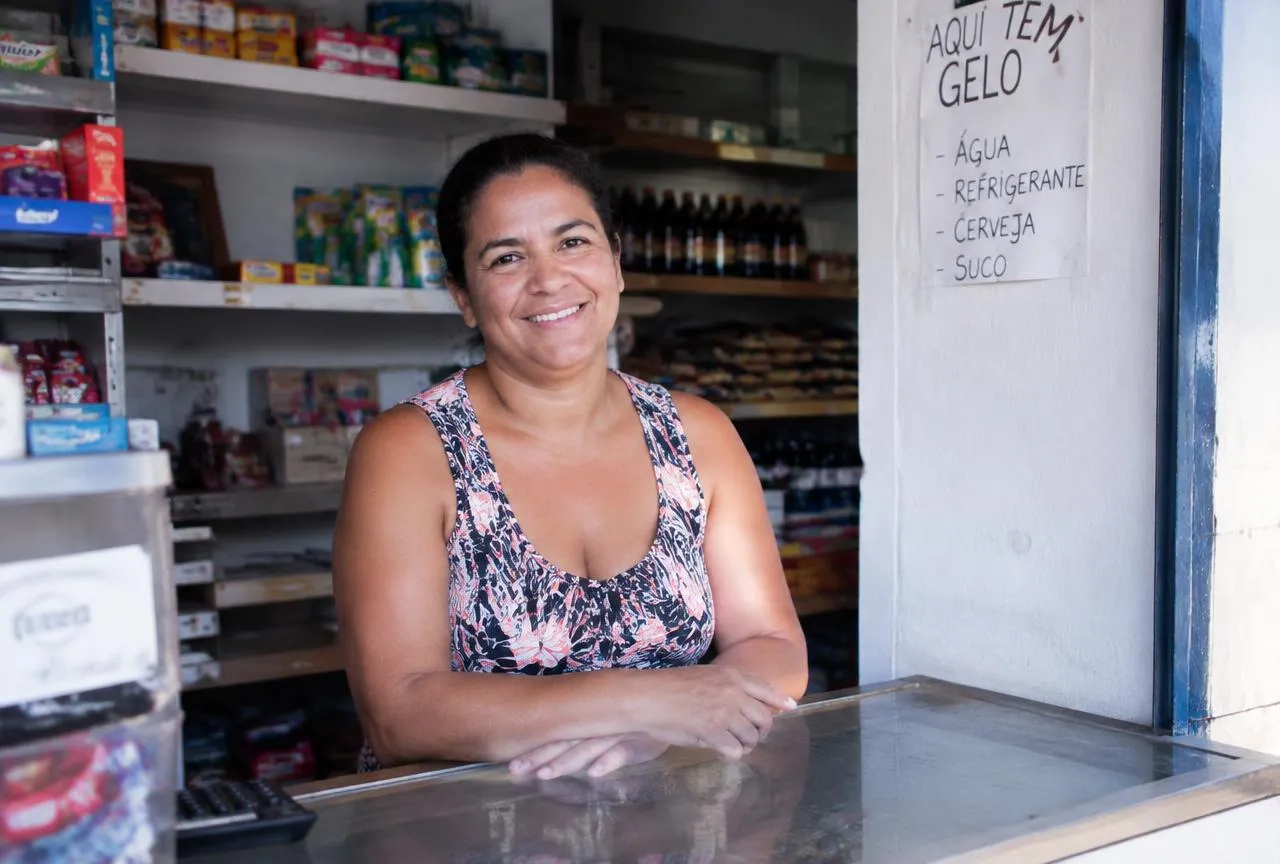 Comerciante sorridente no balcão de sua loja protegida pelo seguro empresarial da Dames
